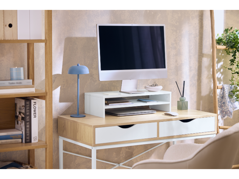 Scrivania da ufficio con computer, supporto monitor, lampada blu e scaffalature in legno.