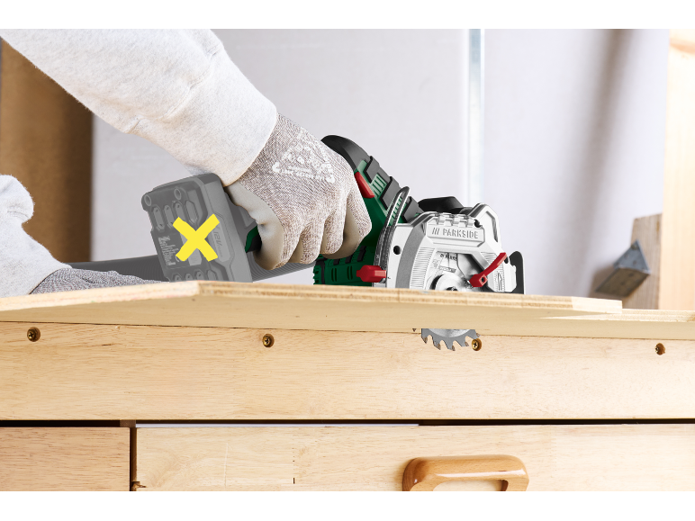 Persona con guanti usa una sega circolare compatta per tagliare un'asse di legno.