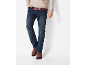 Uomo con maglione beige, camicia a quadri rossa, jeans blu e stivali marroni.
