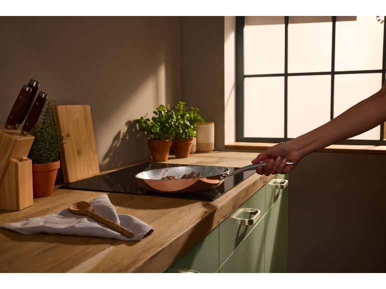 Cucina moderna con padella sul piano cottura, una mano tiene la padella.