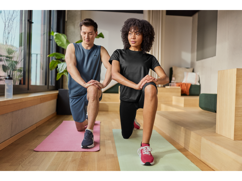 Uomo e donna in abbigliamento sportivo fanno affondi su tappetini da yoga.