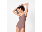 Donna sorridente in canotta e slip color malva, che si lega i capelli.