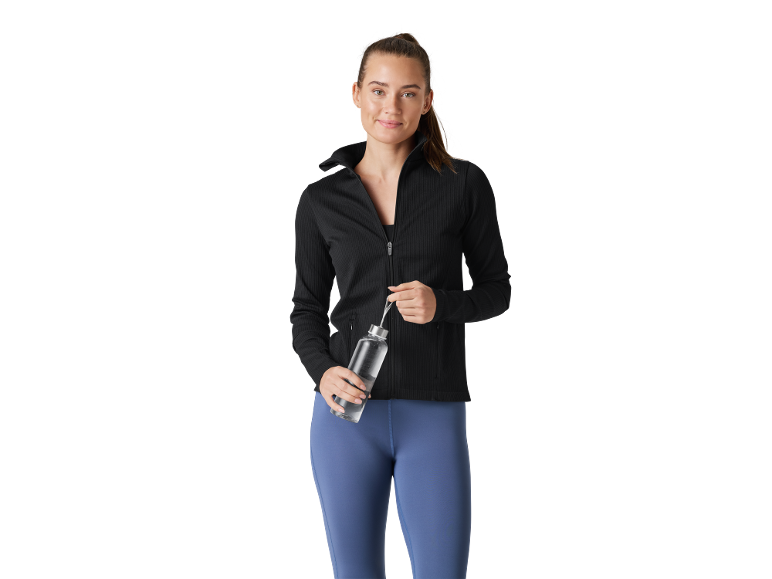 Donna in giacca sportiva nera e leggings blu che tiene una bottiglia d'acqua.