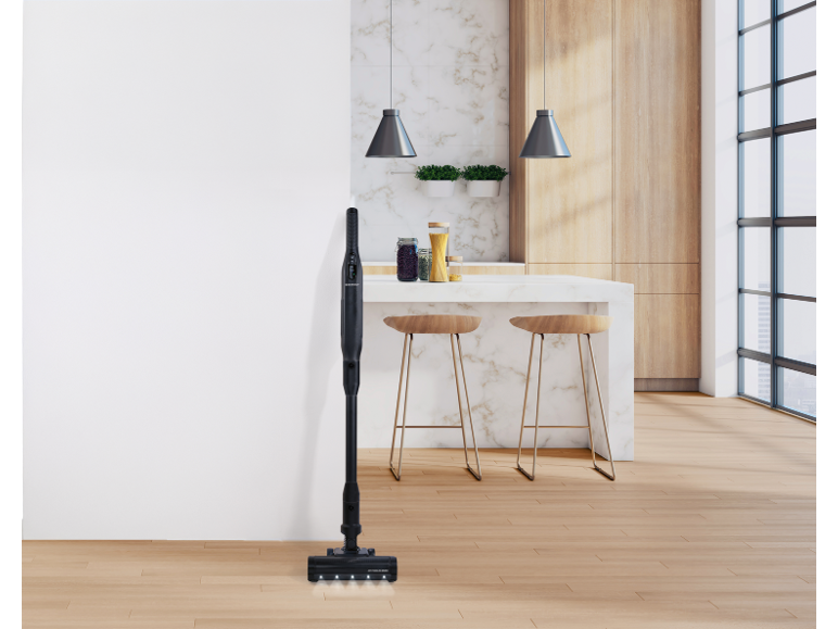 Aspirapolvere a bastone nero in una cucina moderna con pavimento in legno e pareti bianche.