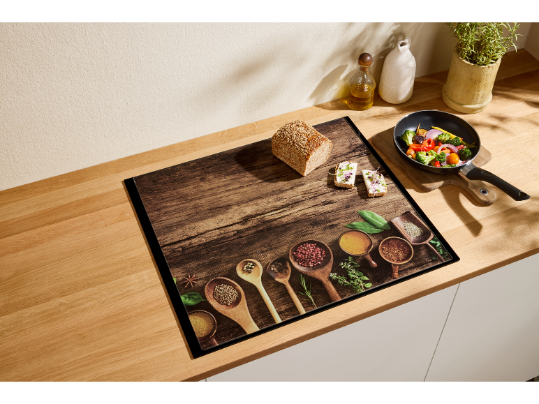 Tagliere in legno con spezie, pane e padella con verdure su un piano di lavoro.