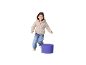 Bambina sorridente con giacca piumino beige e jeans, in piedi accanto a un cilindro viola.