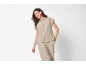 Donna in camicia beige a maniche corte e pantaloni abbinati, sorridente.
