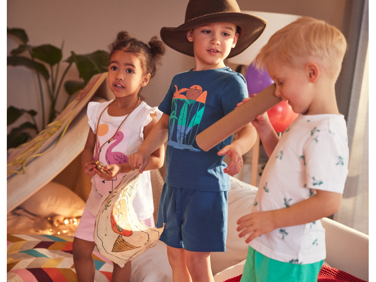 Tre bambini giocano in una tenda, vestiti con abiti estivi.