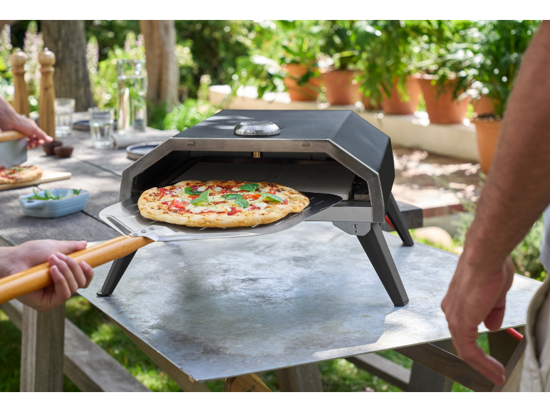 Forno per pizza da esterno con una pizza appena sfornata pronta per essere rimossa con una pala.
