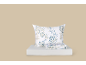 Set di biancheria da letto bianca con motivi floreali blu e beige, include un cuscino e lenzuola piegate.