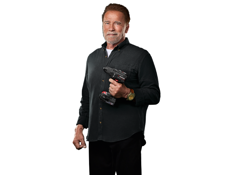 Arnold Schwarzenegger tiene un trapano avvitatore a batteria su sfondo nero.