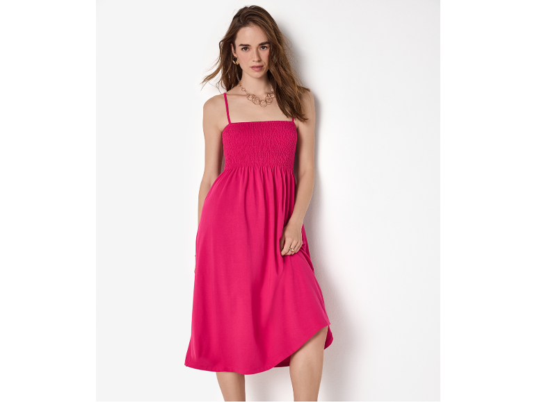 Donna in abito midi fucsia con spalline sottili e corpetto arricciato, con gioielli dorati.