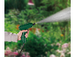 Mano che tiene uno spruzzatore verde che spruzza acqua in un giardino.
