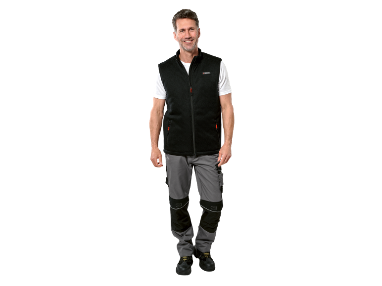 Uomo con gilet in pile nero, maglietta bianca, pantaloni da lavoro grigi e scarpe da lavoro nere.