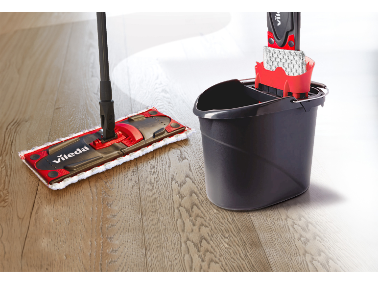 Mocio e secchio con strizzatore su pavimento in legno, pronti per la pulizia.