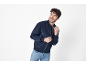 Uomo sorridente con giubbotto bomber blu scuro e jeans.