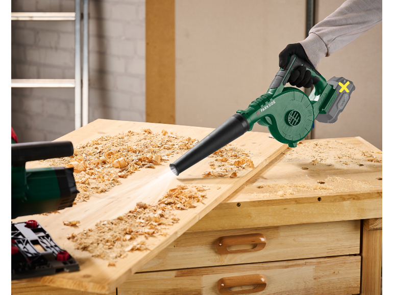 Soffiatore a batteria pulisce trucioli di legno da un banco da lavoro.