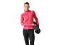Donna in giacca sportiva rosa e leggings neri che tiene un tappetino da yoga arrotolato.