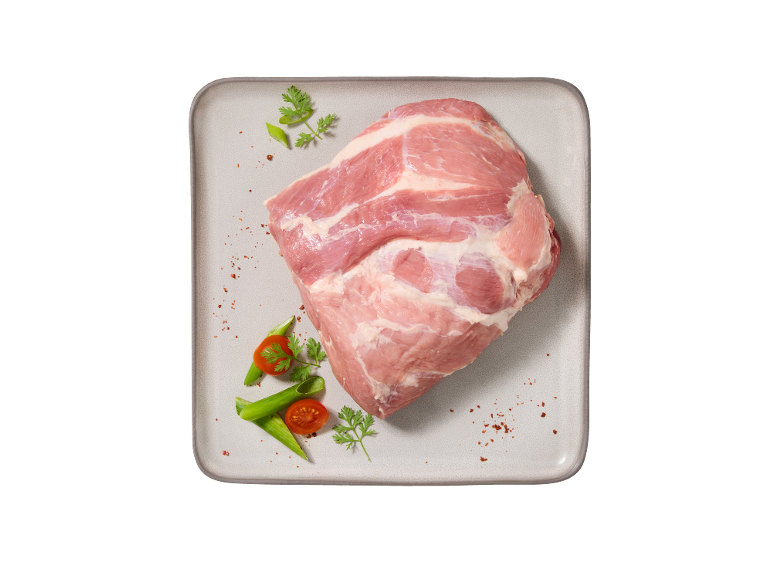 Carne di maiale cruda su un vassoio, guarnita con pomodori, cipollotti e prezzemolo.