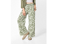 Pantaloni larghi da donna con stampa floreale verde e bianca, abbinati a camicia verde e sneakers beige.