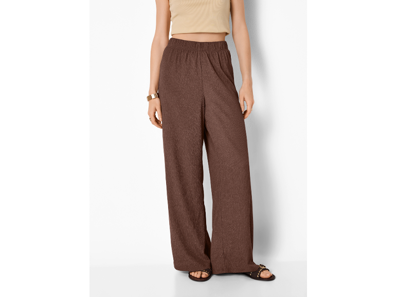 Donna con pantaloni ampi marroni e top corto beige, sandali e bracciale dorato.