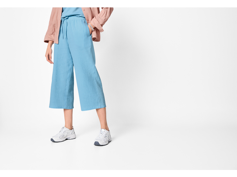 Donna che indossa culotte azzurre, un top abbinato, una camicia rosa e sneakers bianche.