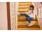 Bambina in jeans e felpa arcobaleno seduta sulle scale, scarpa sul muro.