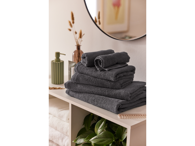 Pila di asciugamani grigi su uno scaffale del bagno con specchio e piante.