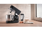 Robot da cucina nero con frusta, farina e uova su un bancone di legno.