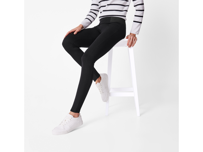 Donna con maglione a righe, leggings neri e scarpe da ginnastica bianche seduta su uno sgabello.