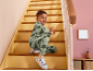 Bambino in tuta verde con dinosauri seduto su una scala di legno.