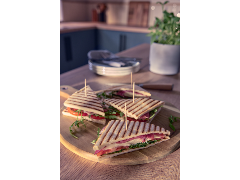 Panini con prosciutto, mozzarella e rucola su un tagliere di legno in cucina.