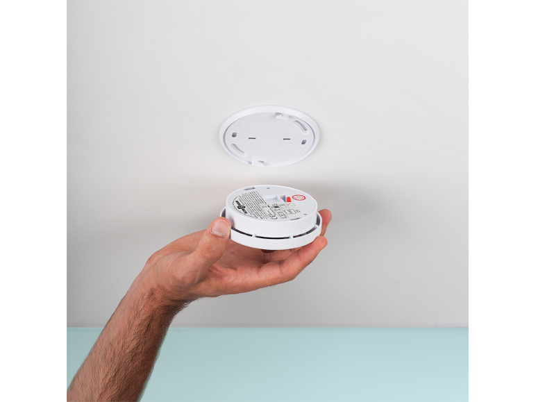 Una mano tiene un rilevatore di fumo, pronto per essere montato a soffitto.