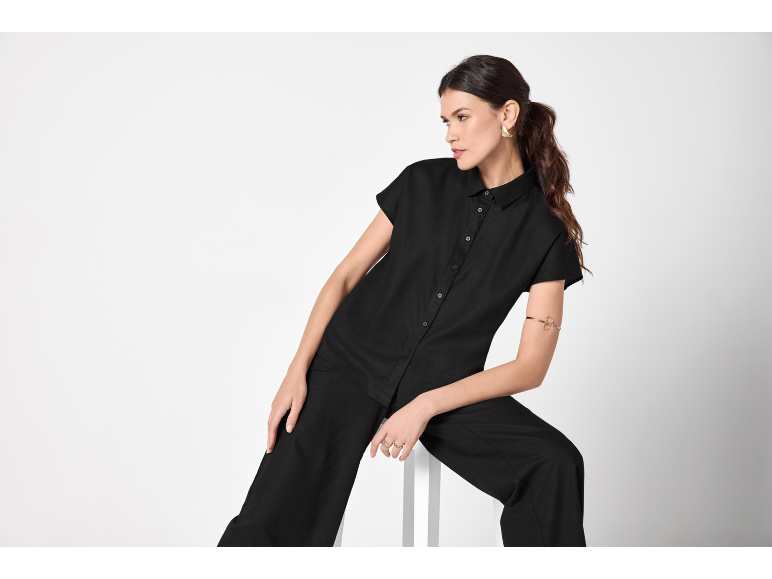 Donna in tuta nera a maniche corte e pantaloni larghi, con orecchini e bracciale dorati.