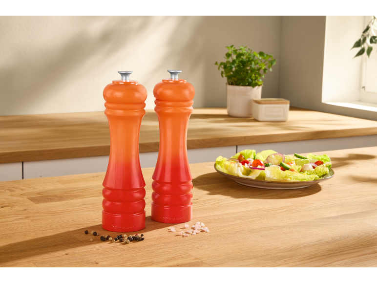 Due macinasale e pepe arancioni e rossi su un bancone da cucina in legno con un'insalata.