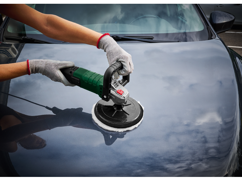 Mani guantate lucidano il cofano di un'auto con una lucidatrice elettrica.
