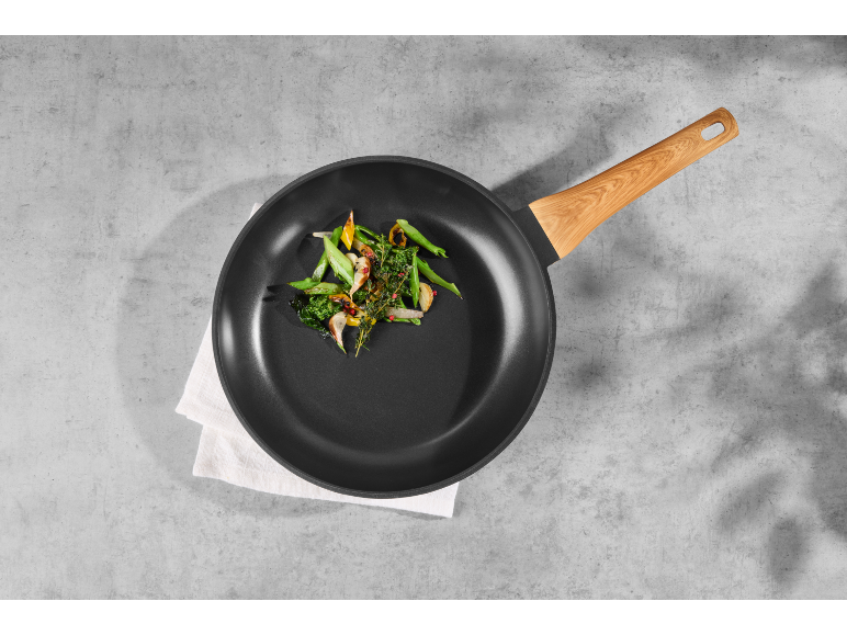 Padella con manico in legno e verdure cotte su sfondo di cemento.
