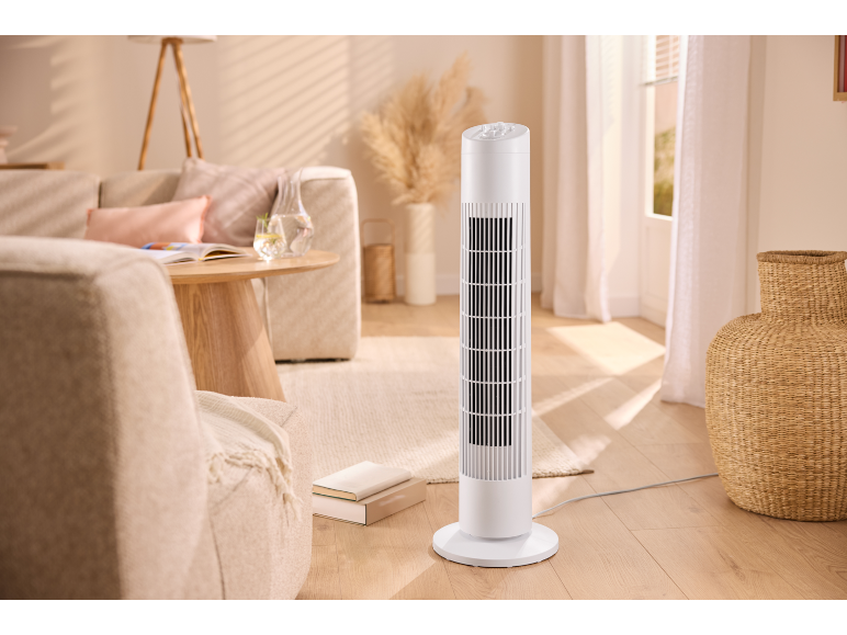 Ventilatore a torre bianco in un soggiorno con divano, tavolo e oggetti decorativi.