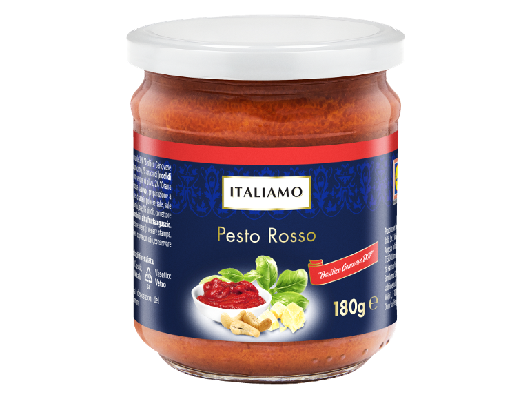 Vasetto di pesto rosso etichettato 'Pesto Rosso', circondato da basilico, anacardi e formaggio.