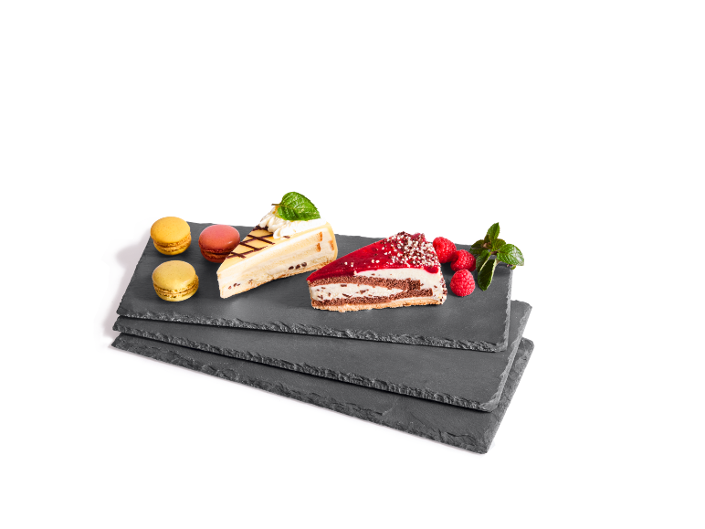 Fette di torta e macarons su vassoi di ardesia, guarniti con lamponi e menta.