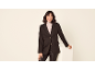 Donna con blazer nero, pantaloni in pelle e dolcevita beige, sorridente.