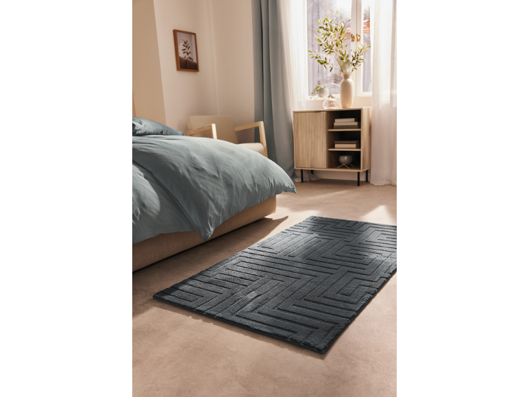Camera da letto con letto, tappeto blu e mobile in legno accanto alla finestra.