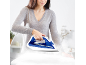 Donna che stira vestiti bianchi con un ferro da stiro a vapore blu e bianco.