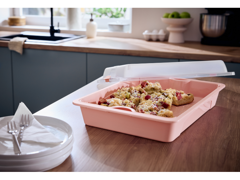 Torta di rabarbaro in contenitore rosa con coperchio, con piatti e posate in cucina.