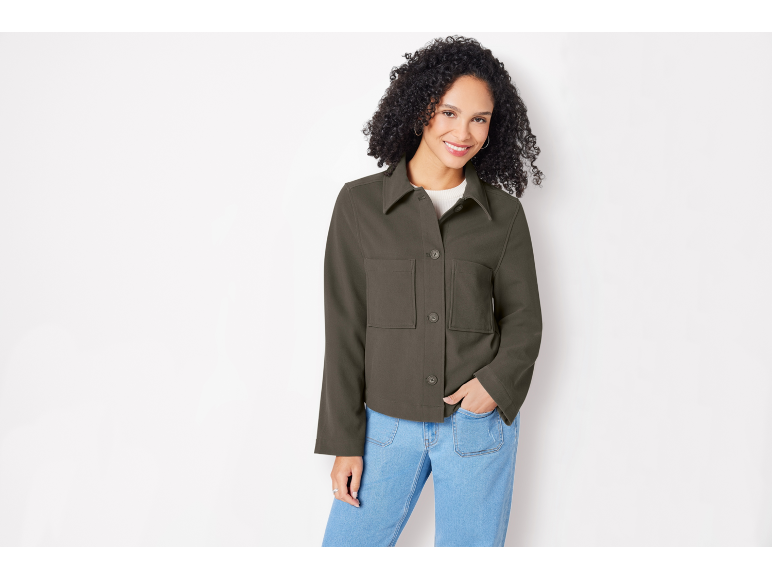 Donna con giacca verde militare e jeans blu, sorridente alla fotocamera.