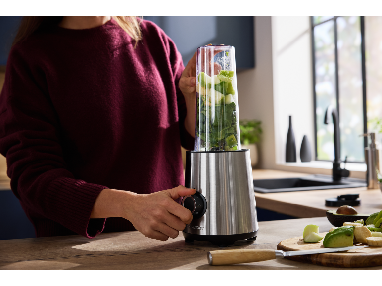 Donna che prepara un frullato verde con un frullatore in cucina.