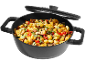 Una pentola nera piena di gnocchi, zucchine, funghi e pomodori, con un coperchio sopra.