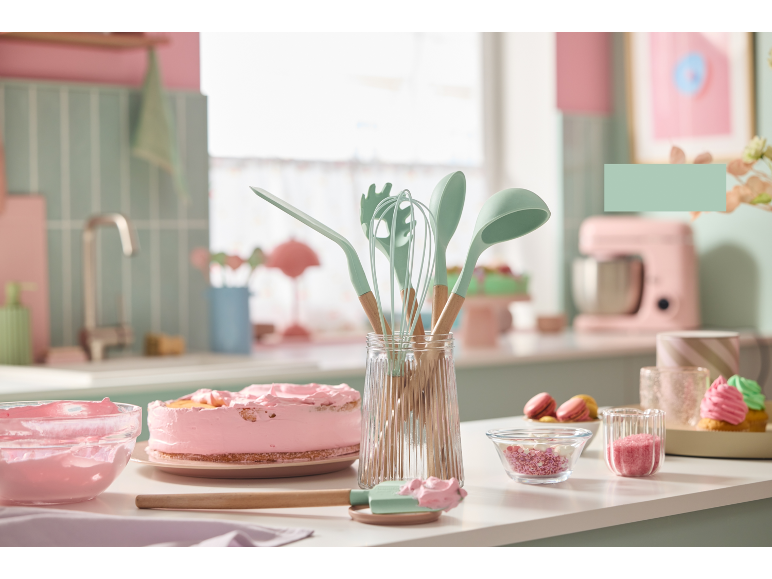 Utensili da cucina e torta rosa in una cucina dai toni pastello.