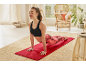 Donna in reggiseno sportivo nero e leggings fantasia che fa yoga su un tappetino rosso.