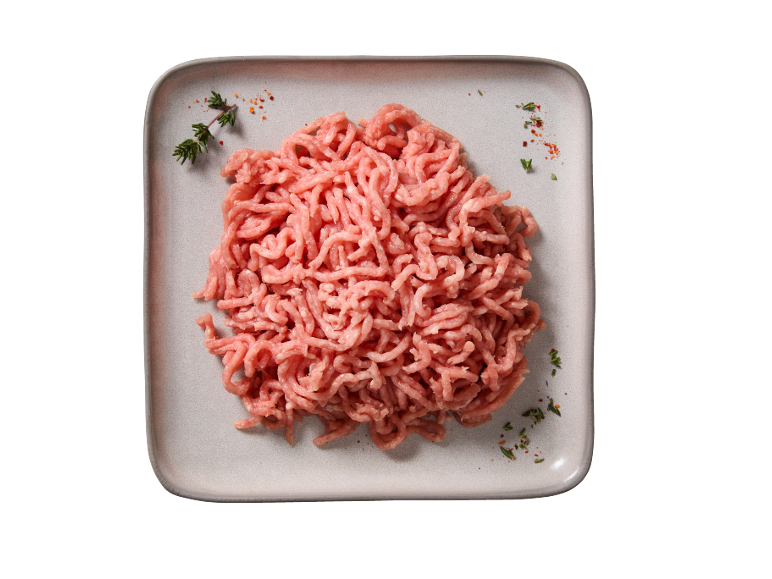 Carne macinata cruda su un piatto grigio chiaro, guarnita con erbe e spezie.